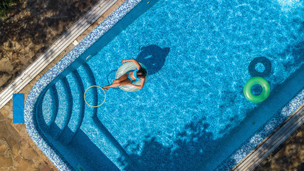 Aerial view of beautiful girl in swimming pool from above, swim on inflatable ring donut and has fun in water on family vacation on tropical holiday resort