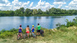 © Iuliia Sokolovska - Family on bikes cycling outdoors, active parents and kids on bicycles, aerial view of happy family with children relaxing near beautiful river from above, sport and fitness concept