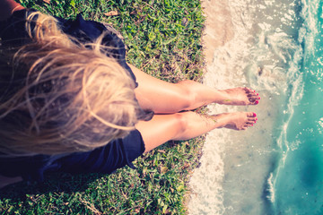 Wall Mural - A girl hung her legs on the edge of a cliff sits above the ocean.