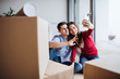 © Halfpoint - Young couple with cardboard boxes moving in a new home, taking selfie.