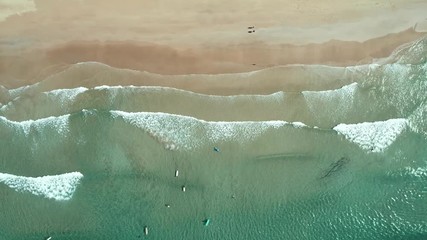 Wall Mural - Top view of waves break on tropical white sand beach and surfers with surfing boards. Aerial drone view 4k shot of sea waves on the beautiful beach.