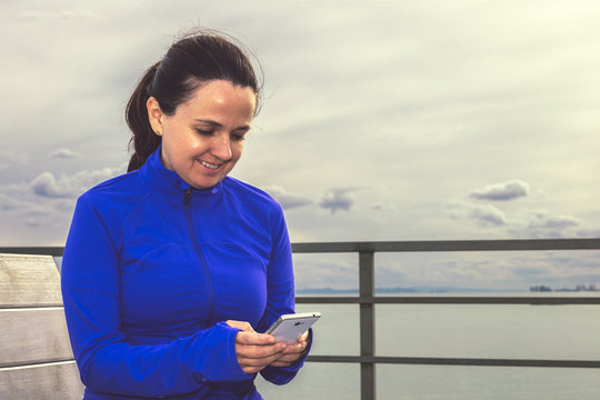 Mujer deportista sonriendo Escribiendo Mensaje con Teléfono Móvil con el mar de fondo