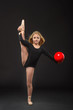 Cute little ballerina with long hair in a black leotard and pointe posing on a black background