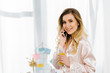 © LIGHTFIELD STUDIOS - Attractive woman in satin pyjamas talking on smartphone and drinking orange juice
