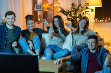 Friendship, Leisure, People And Entertainment Concept - Happy Friends Watching Tv At Home In Evening