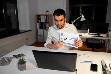 Canvas Print - business, technology and people concept - businessman with charts having video chat on laptop computer at night office