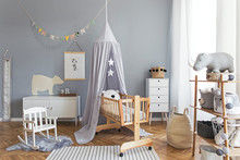 Stylish And Bright Scandinavian Decor Of  Newborn Baby Room With Mock Up Poster, White Design Furnitures, Natural Toys, Hanging Grey Canopy With Wooden Cradle, Bookstand, Accessories And Teddy Bears. 