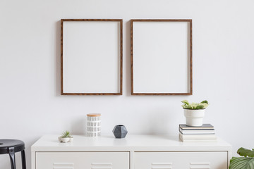 Minimalistic home decor of interior with two brown wooden mock up photo frames on the white shelf with books, beautiful plant in stylish pot, box and home accessories. White walls. Mockup concept.