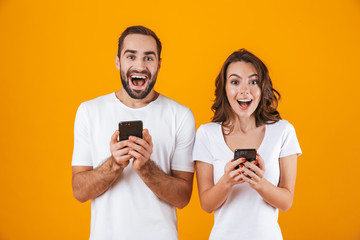 Poster - Image of beautiful couple man and woman smiling while both using mobile phones, isolated over yellow background