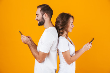 Canvas Print - Image of modern couple man and woman smiling while both using mobile phones, isolated over yellow background