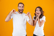 © Drobot Dean - Portrait of attractive couple man and woman in basic clothing pointing fingers, while standing together isolated over yellow background