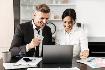 Handsome business man work indoors with his colleague woman with documents and laptop computer.