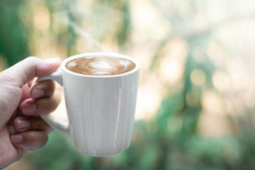 Wall Mural - Hand holding coffee cup on bokeh nature background