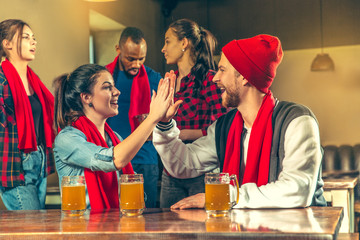 Sport, people, leisure, friendship, entertainment concept - happy male and female football fans or good young friends drinking beer, celebrating victory at bar or pub. Human positive emotions concept