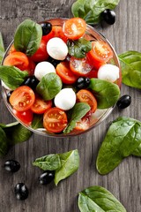 Fresh tomato, cheese and spinach salad on wooden background. Healthy diet.