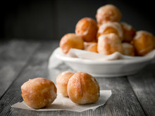 Small Homemade Doughnuts, Also Known As Doughnut Holes, Prepared For Polish Fat Thursday. On The Foreground Three Doughnuts On A Piece Of Baking Paper, In The Background A White Bowl Full Of Doughnuts