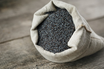 Poppy seeds in a burlap bag on a vintage wooden gray background. The tasty and useful seeds rich with protein and oils.