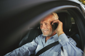 Wall Mural - Smiling senior man driving his car talking on a cellphone