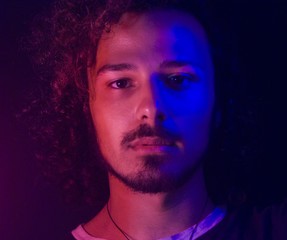 Portrait normal latin young man expresive looking at the camera with red and blue light. Facial hair: moustache, beard