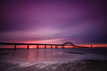 Wall Mural - Sweeping pastel colored clouds sweeping across a pre dawn sky, with a bridge crossing a body of water. Fire Island Inlet Bridge - Long Island New York. 