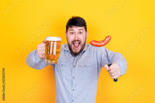 Fotografía man with a glass of beer and grilled sausage on a fork in his hand, standing on