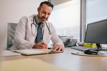 Wall Mural - Doctor writing in his diary sitting at clinic desk