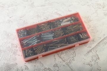 Screws in red storage box on white cement background.