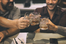 Close Up Of Unrecognizable Men Clinking Crystal Glasses With Alcoholic Beverage. Clients Of Bar Or Pub Enjoying Their Drinks Such As Whiskey, Rum, Scotch Or Brandy.