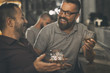 Two male friends spending time together in bar and having fun. Bearded men smiling, looking at each other and communicating. Men holding crystal glasses of whisky or scotch.