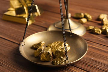 Scale pan with gold lumps on wooden table, closeup