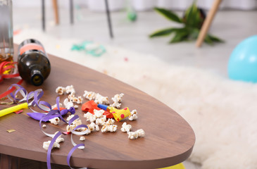 Messy table with popcorn, streamers and bottle after party indoors