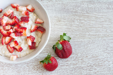 Top view of rolled  organic porridge with cut strawberries and two whole berries in marble bowl half is shown on wooden table  healthy breakfast