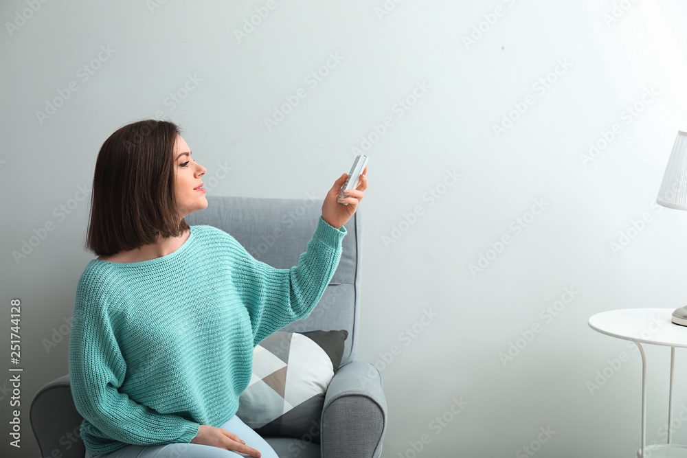 Young woman switching on air conditioner at home