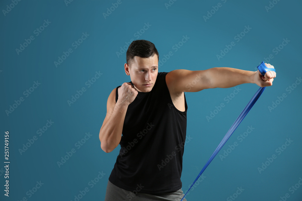 Sporty young man training with resistance band against color background