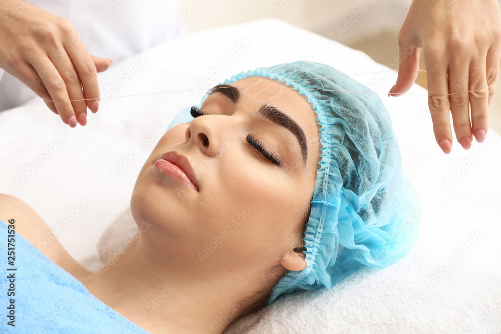 Young woman undergoing eyebrow correction procedure in beauty salon