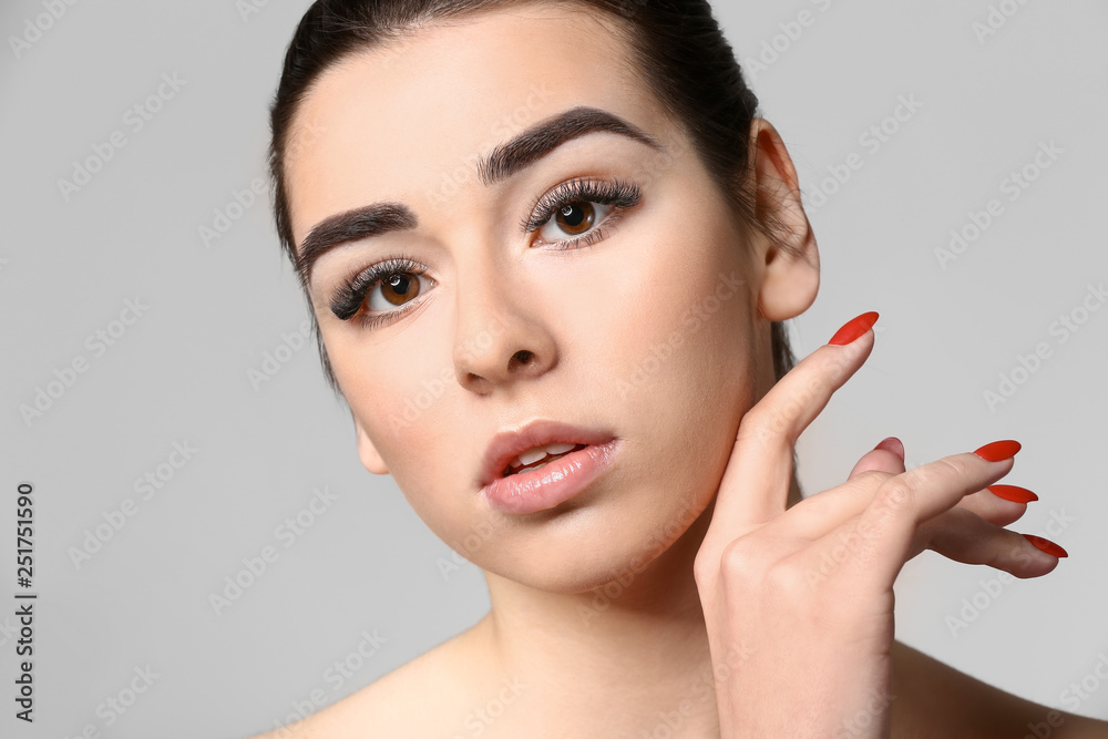 Young woman with beautiful eyebrows on grey background