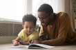 © fizkes - Happy black father and toddler son reading book at home