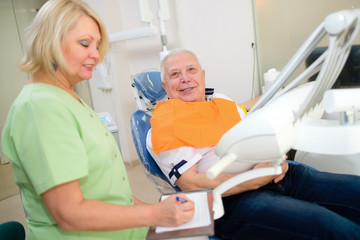 female dentist talking with smiling senior man patient at dental clinic. dental care for elder peopl