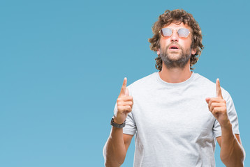 Sticker - Handsome hispanic model man wearing sunglasses over isolated background amazed and surprised looking up and pointing with fingers and raised arms.