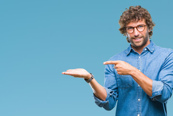 Sticker - Handsome hispanic model man wearing glasses over isolated background amazed and smiling to the camera while presenting with hand and pointing with finger.