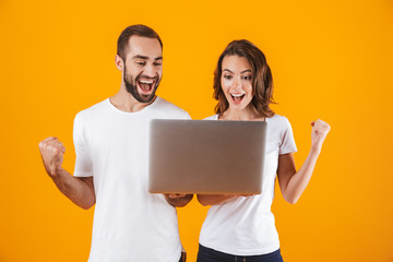 Wall Mural - Portrait of successful man and woman holding silver laptop, while standing isolated over yellow background