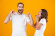 © Drobot Dean - Portrait of caucasian couple man and woman in basic clothing pointing fingers, while standing together isolated over yellow background