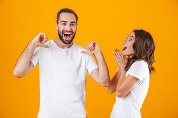 Sticker - Portrait of caucasian couple man and woman in basic clothing pointing fingers, while standing together isolated over yellow background