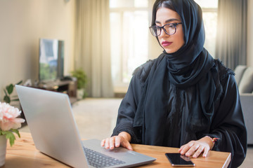 Young arab woman wearing hijab working on laptop at home.