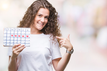 Poster - Young brunette girl holding menstruation calendar over isolated background with surprise face pointing finger to himself