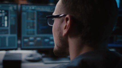 Aufkleber - Portrait of IT Specialist Wearing Glasses Works on Personal Computer with Screens Showing Software Program with Coding Language Interface. Dark Colors. Close-up Moving Shot