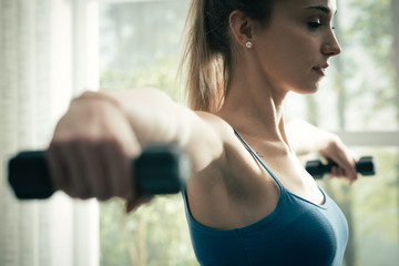 Young sporty woman exercising with dumbbells at home