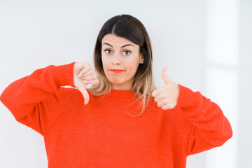 Sticker - Young woman wearing casual red sweater over isolated background Doing thumbs up and down, disagreement and agreement expression. Crazy conflict