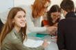 © Nestor - Portrait of happy smiling girl with long hair sitting near table. Students communicating and discussing interesting topic. Pupils during interactive lessons in private school of foreign languages.