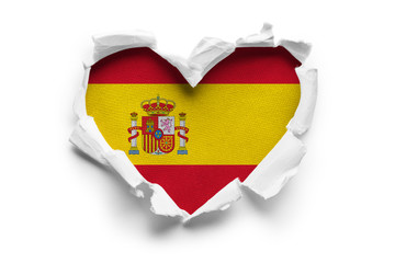 Heart shaped hole torn through paper, showing satin texture of flag of Spain. Isolated on white background